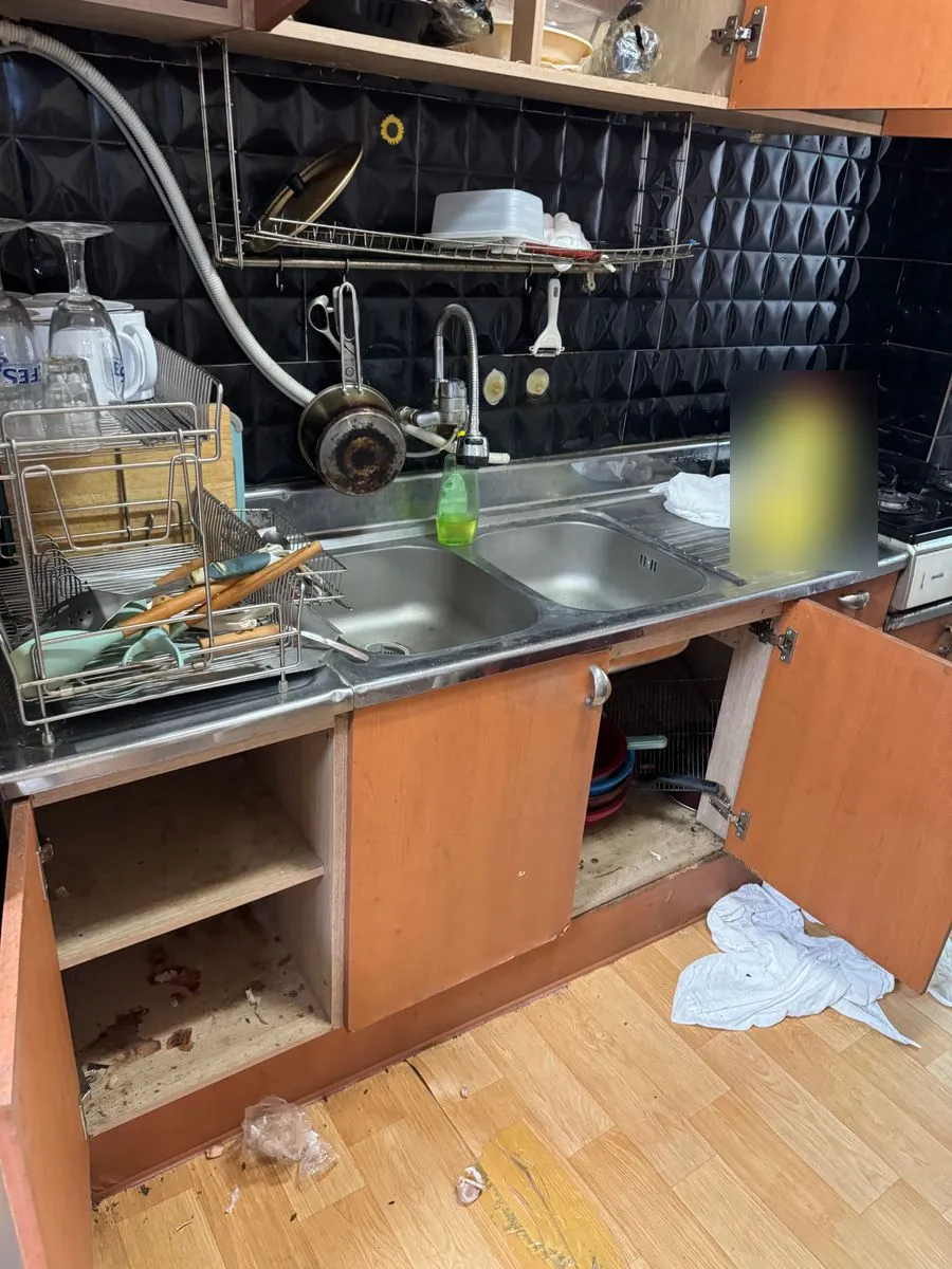 안산 쓰레기집 청소 작업 전 개수대 아래 수납장 문이 열리고 바닥에 얼룩과 부스러기가 남은 주방