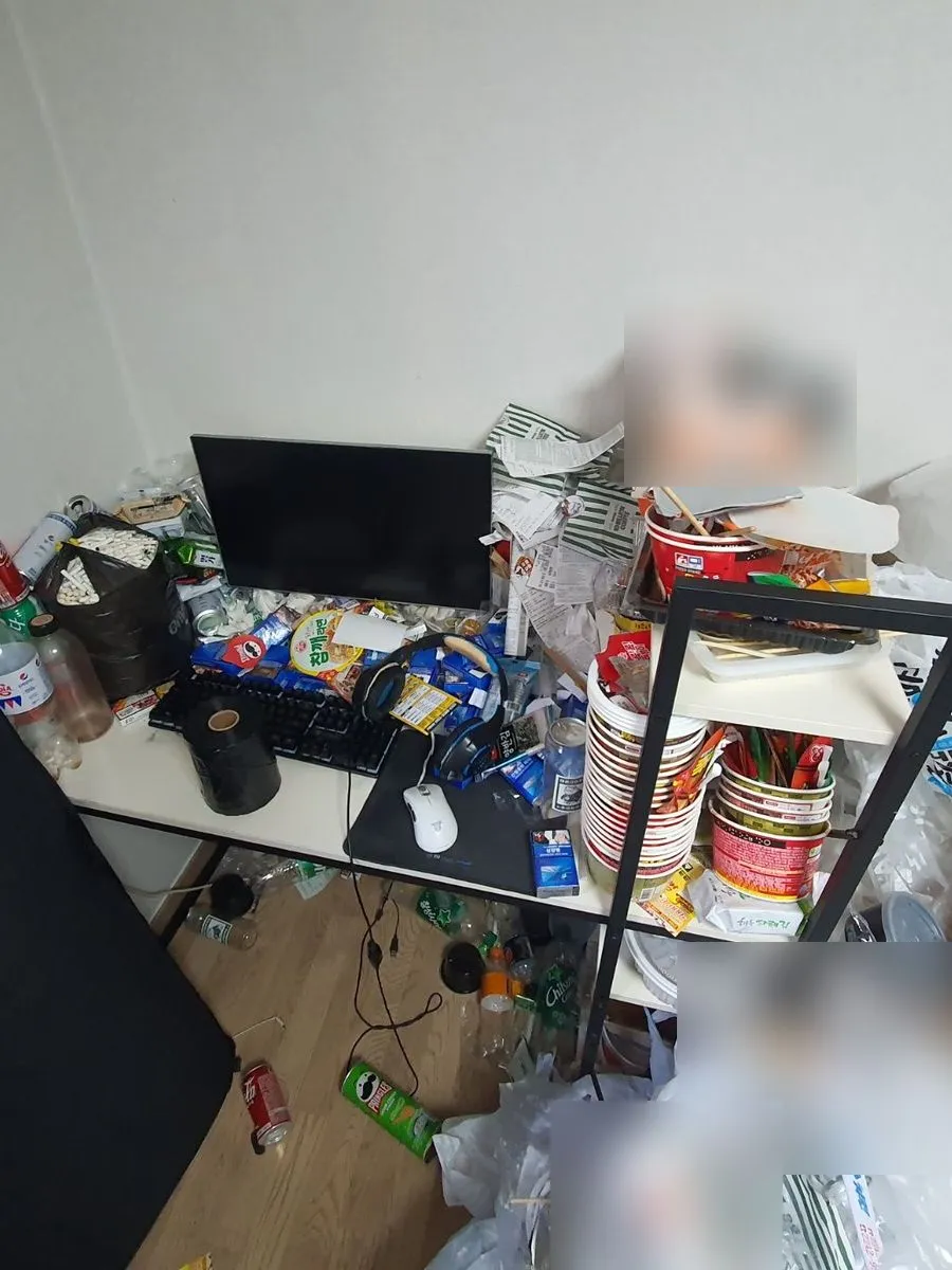 안양 쓰레기집 청소 작업 전 책상 위와 옆 선반에 음식 용기와 봉지가 쌓인 모습